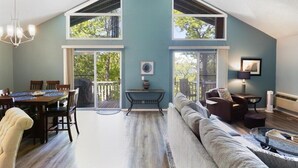 A spacious living area with a high ceiling, large windows, a dining table, and a cozy seating area. - Margaritaville house next to pool (Osage Beach)