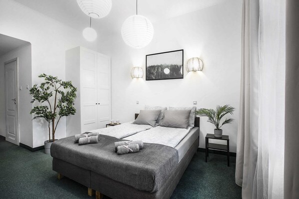 A modern bedroom with a large bed, two bedside tables, a potted plant, and a framed picture on the wall.