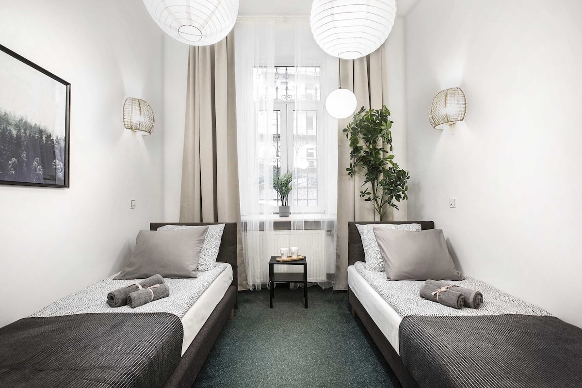 Ein Hotelzimmer mit zwei Betten, einem kleinen Tisch, einer Pflanze und einem Fenster mit Vorhängen.