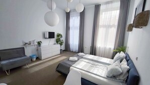 A modern bedroom with a bed, a sofa, a TV, a dresser, and a plant. - Bedrouse Czapskich 5 - Old Town (Kraków)