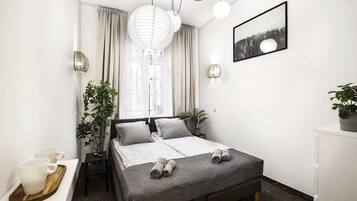 A modern bedroom with a bed, bedside tables, a window with curtains, a wall-mounted picture, and a potted plant.