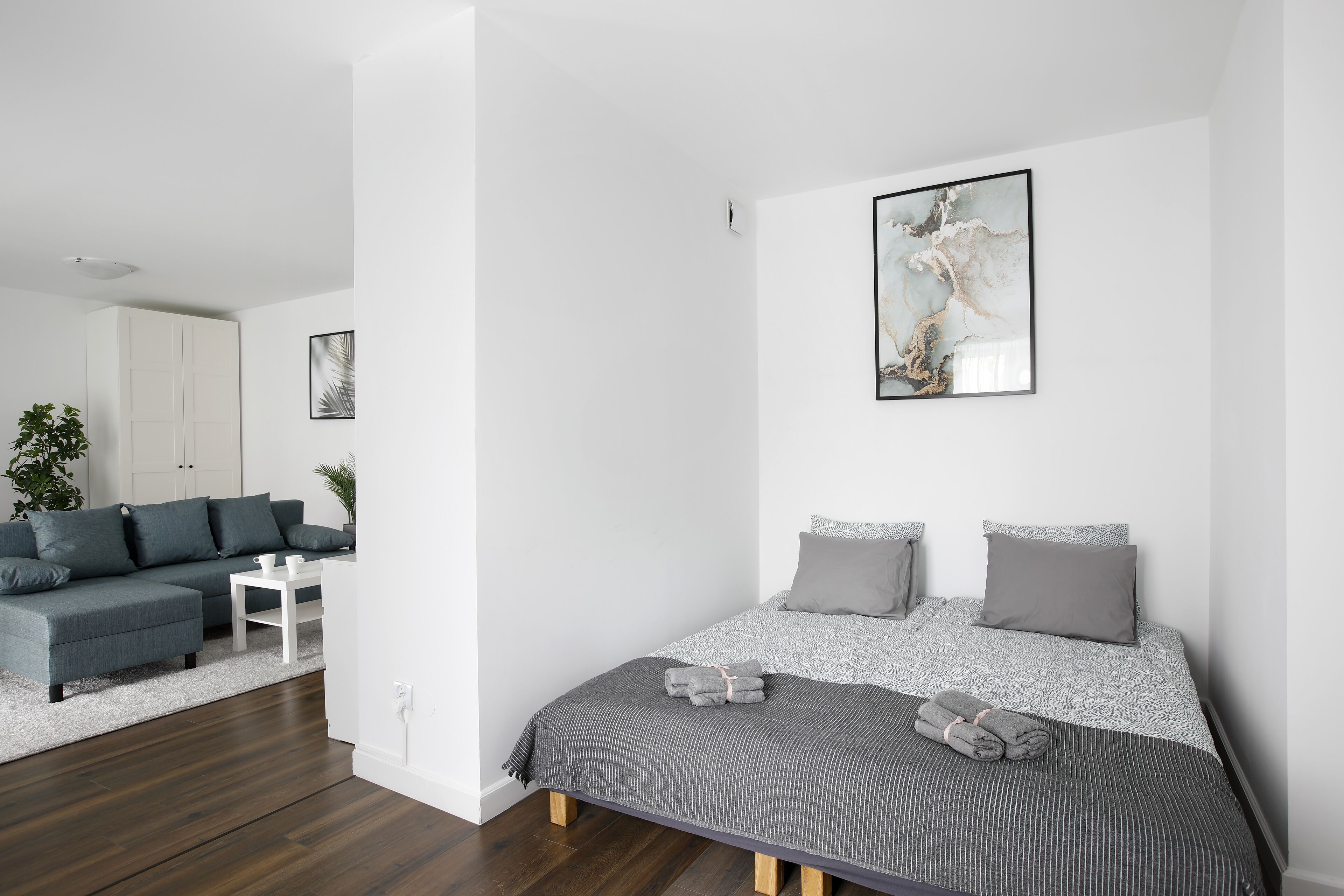 Una camera da letto moderna con un letto, biancheria grigia, un divano grigio, un piccolo tavolino bianco e un grande quadro astratto appeso alla parete.