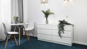 A modern room with a white dresser, two wall-mounted lights, a potted plant, and a dining area with a white table and chairs. - Bedrouse Czapskich 5 - Old Town (Kraków)