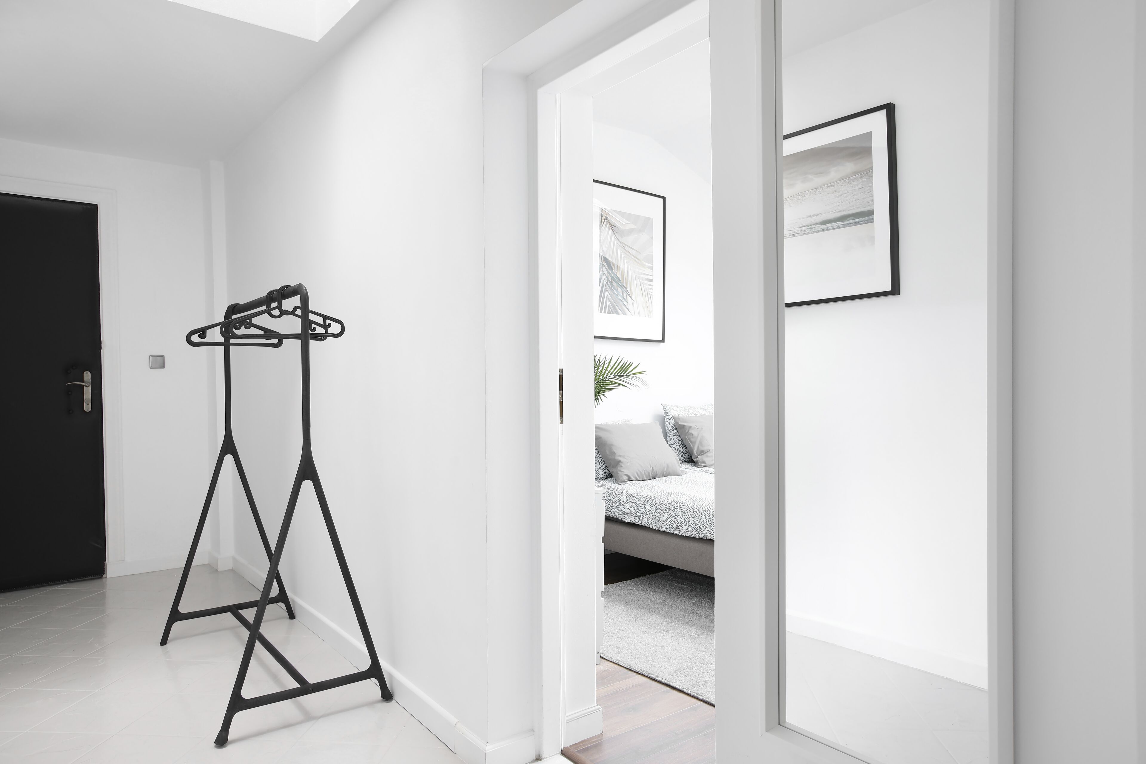 Una habitación moderna y minimalista con un perchero de metal negro, una cama con edredón gris y blanco, y un cuadro abstracto enmarcado en la pared.