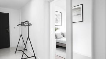 Una habitación moderna y minimalista con un perchero de metal negro, una cama con edredón gris y blanco, y un cuadro abstracto enmarcado en la pared.