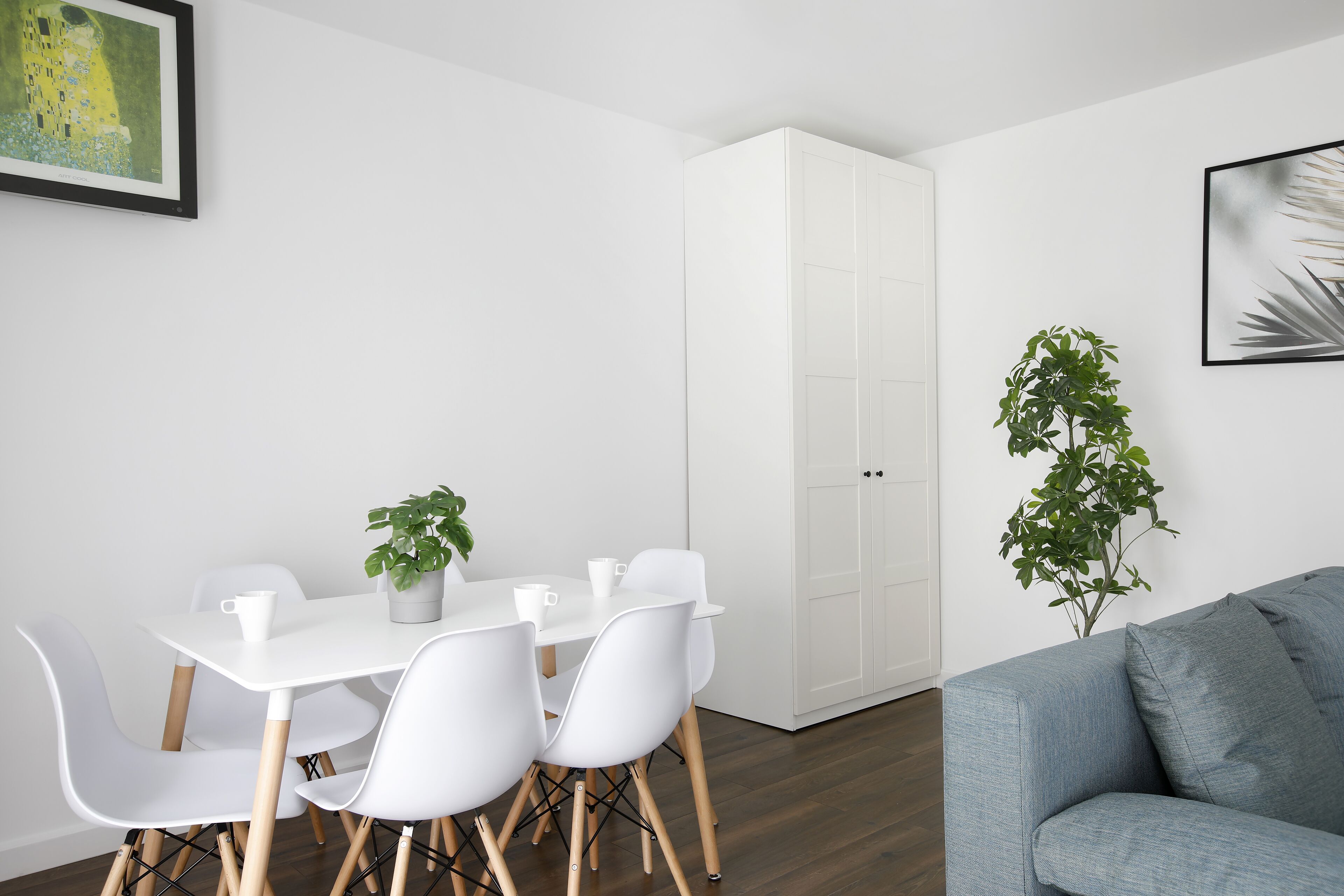 A modern room with a white dining table, white chairs, a grey sofa, and a white wardrobe.