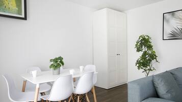 A modern room with a white dining table, white chairs, a grey sofa, and a white wardrobe.