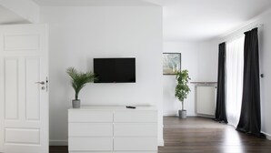 A modern living room with a white entertainment unit, a flat-screen TV, and two potted plants. - Bedrouse Czapskich 5 - Old Town (Kraków)