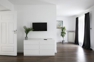 Un soggiorno moderno con un mobile TV bianco, un televisore piatto e due piante in vaso.