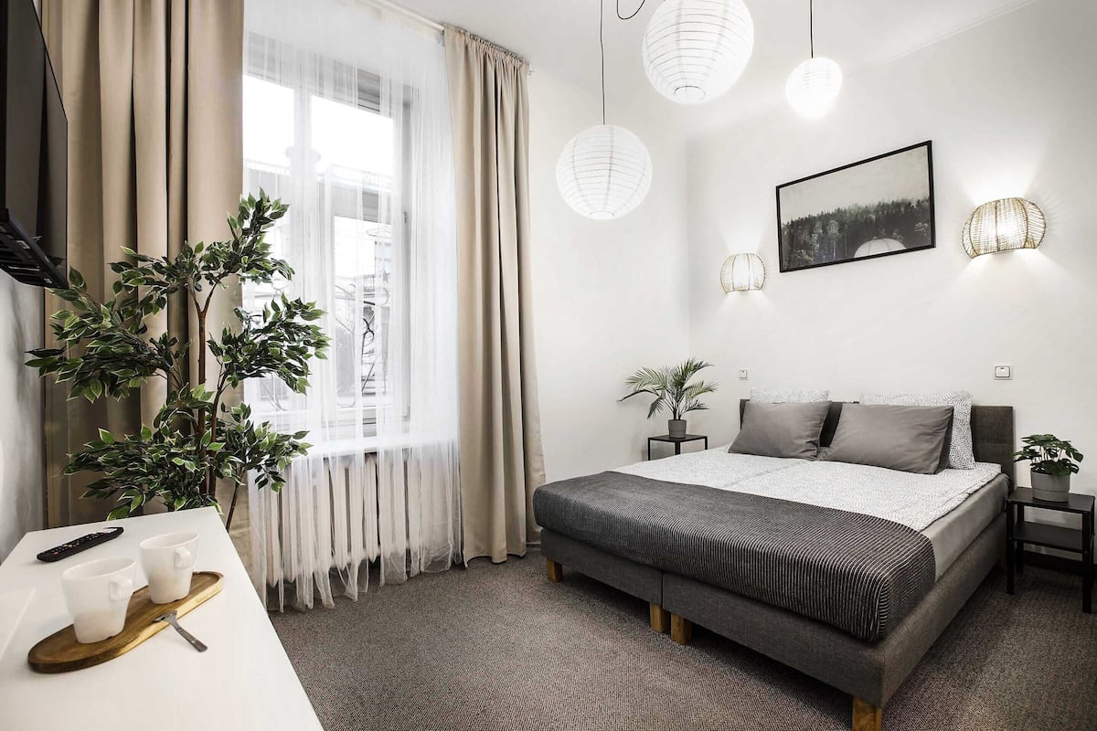 Ein modernes Hotelzimmer mit einem großen Bett, Nachttischen, einem Schreibtisch mit Fernbedienung und einer Topfpflanze.