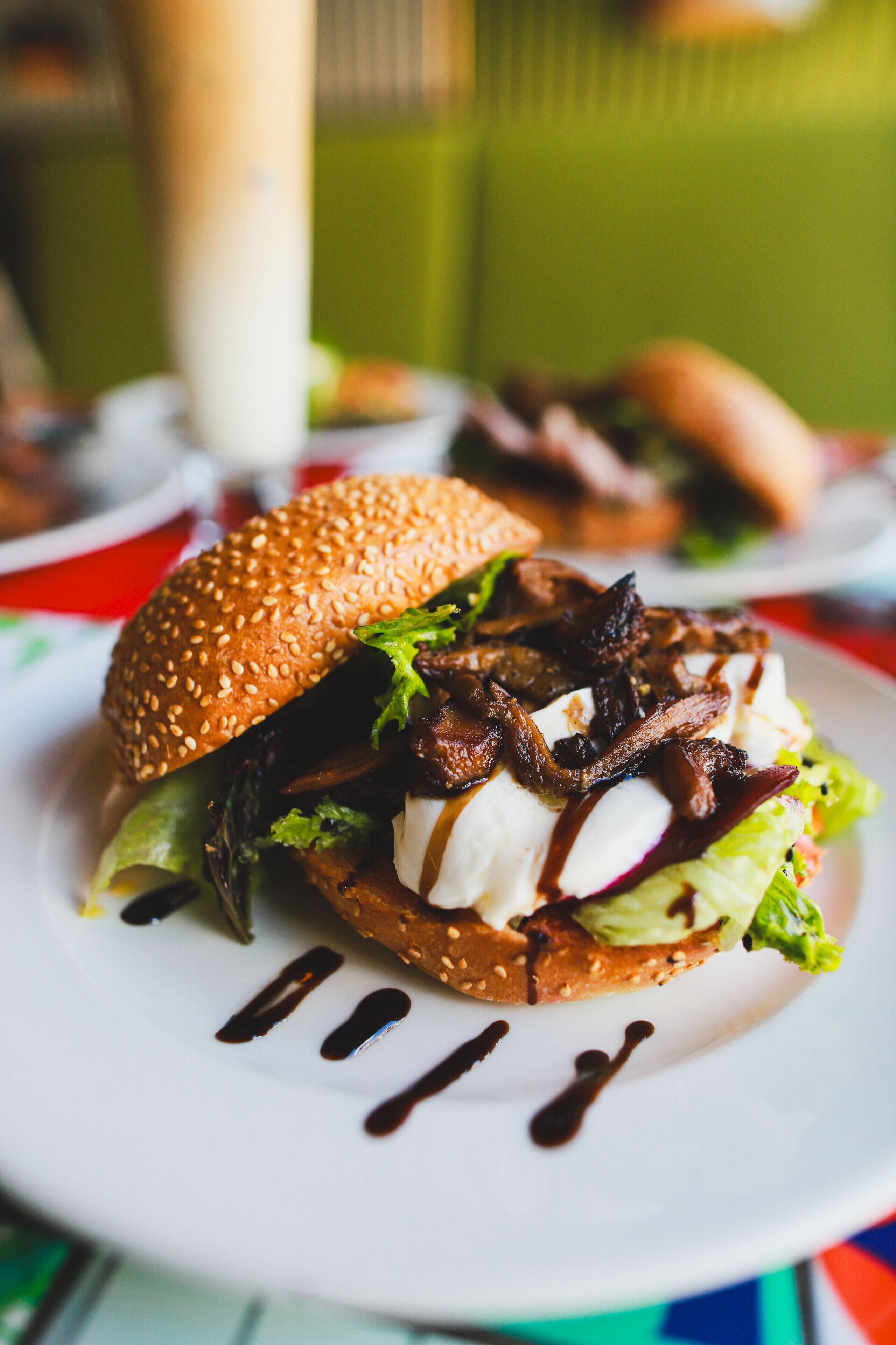 A sandwich with sesame seed bun, lettuce, and a drizzle of sauce on a white plate.