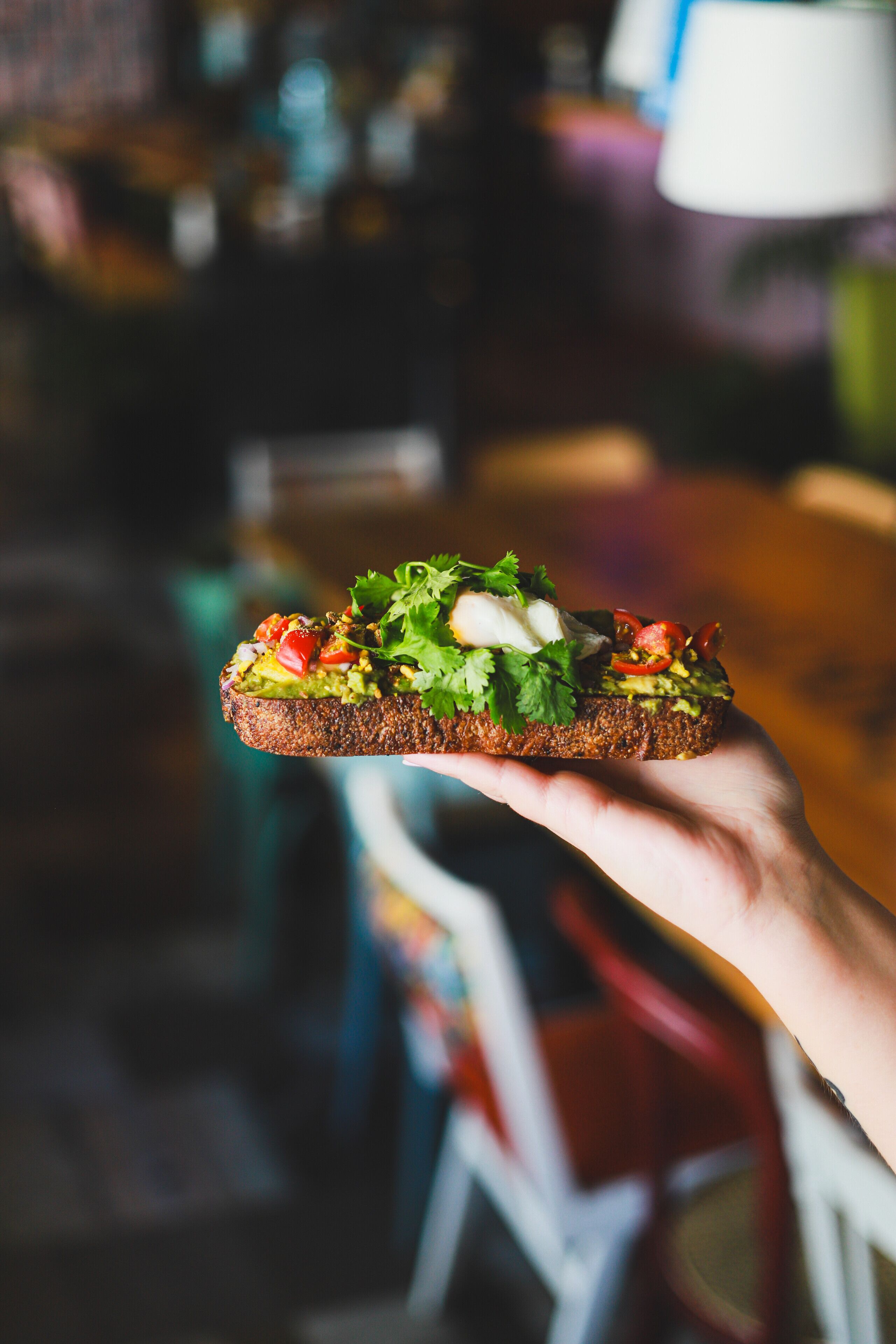 Une main tenant une tranche de pain grillé garnie d’avocat, de tomates et de laitue.