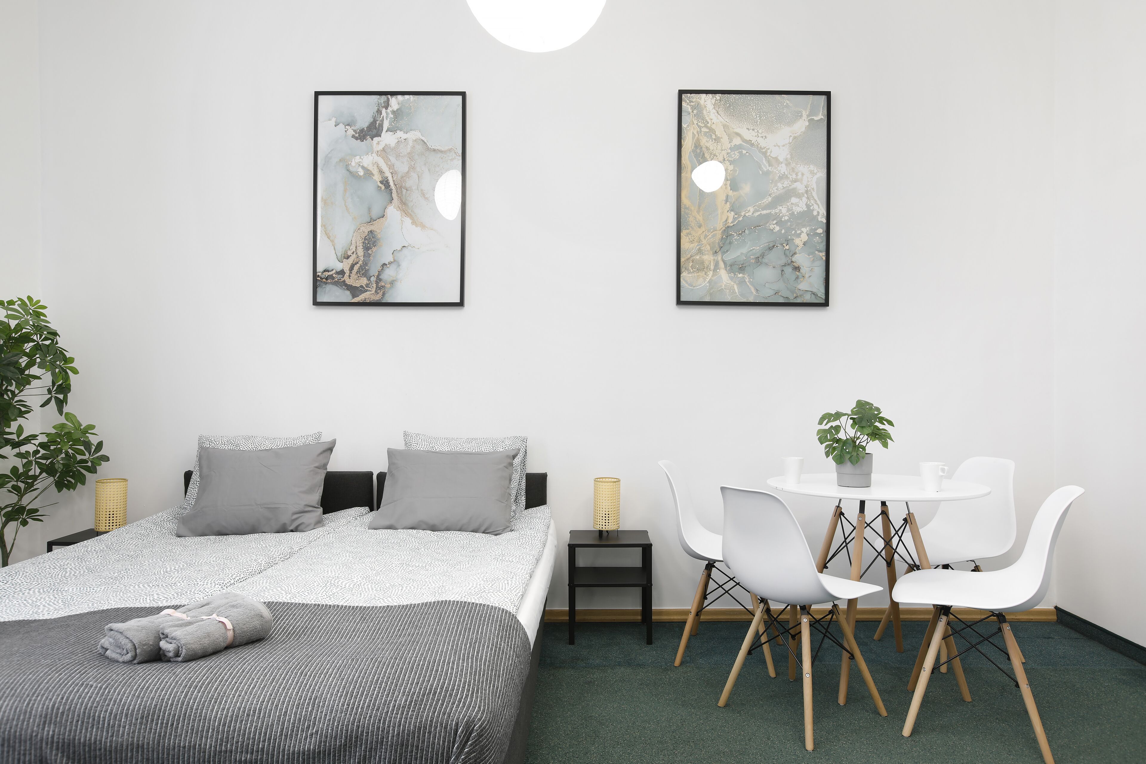 Ein modernes Hotelzimmer mit einem ordentlich bezogenen Bett, einem kleinen Esstisch mit Stühlen und zwei abstrakten Bildern an der Wand.