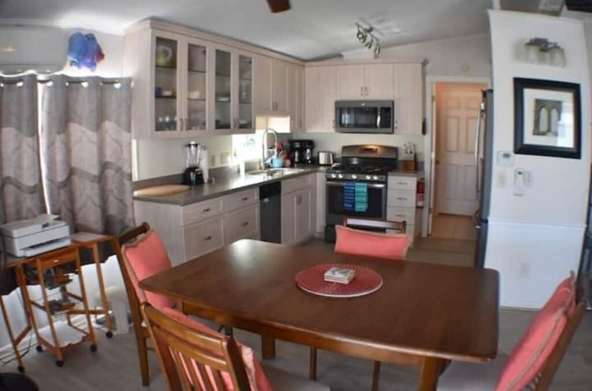 A compact kitchen with a microwave, stove, and cabinets. There is a dining table with chairs and a printer on a cart.