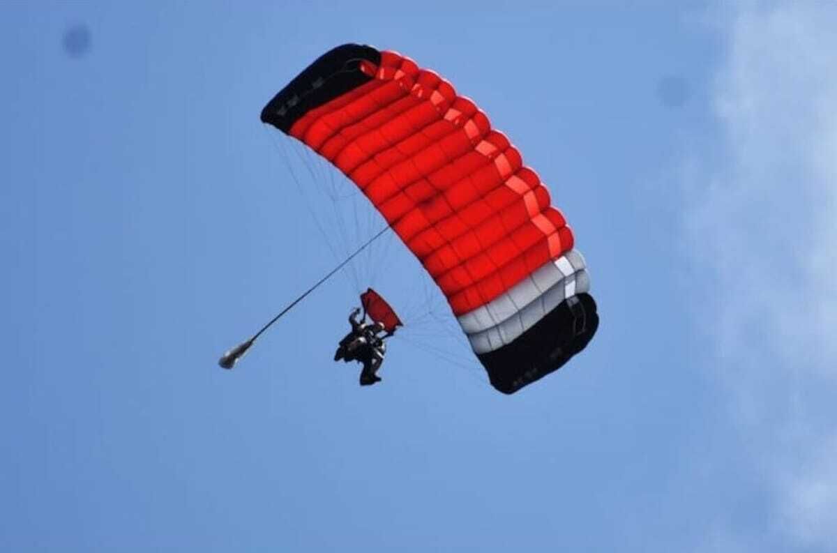 Un parapentista con un paracaídas rojo, blanco y negro frente a un cielo azul despejado.