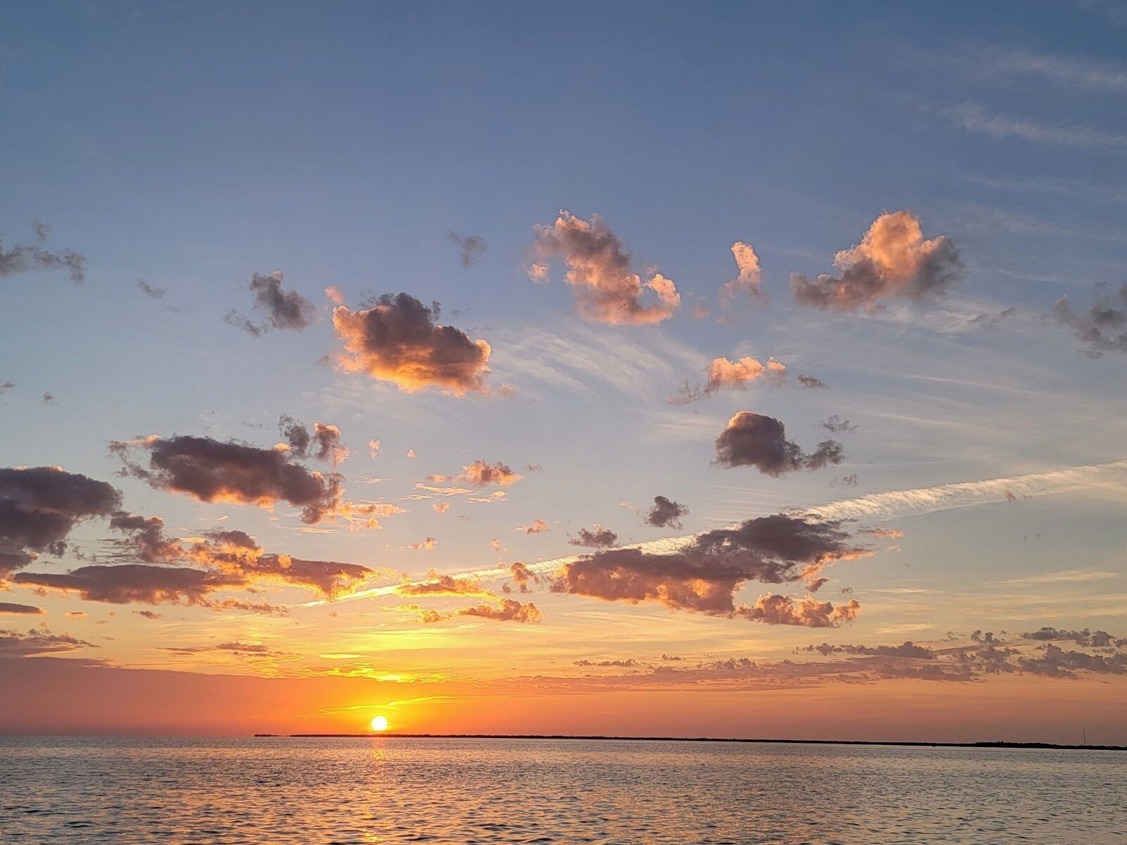 A sunset over a calm sea with scattered clouds.