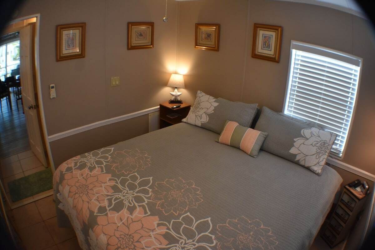 A bedroom with a large bed, a nightstand with a lamp, and framed pictures on the wall.
