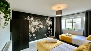 A hotel room with two beds, a large floral mural on the wall, a window with curtains, and a radiator. - Curzon House 2 (Cleethorpes)