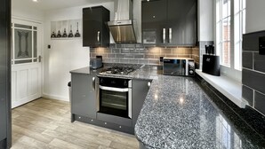 A modern kitchen with granite countertops, stainless steel appliances, and a large window providing natural light. - Curzon House 2 (Cleethorpes)