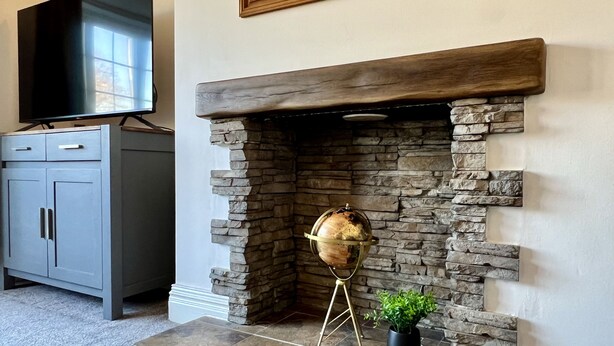 A stone fireplace with a globe, a television above it, and a grey cabinet to the left. - Curzon House 2 (Cleethorpes)