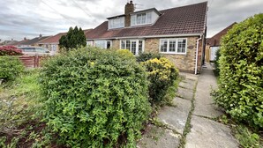 A two-story house with a tiled roof, a visible chimney, and a front garden with various shrubs and a pathway leading to the entrance. - Curzon House 2 (Cleethorpes)