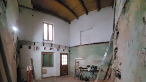 Una habitación con suelo de baldosas, una puerta de madera, una ventana y una escalera apoyada en la pared.
