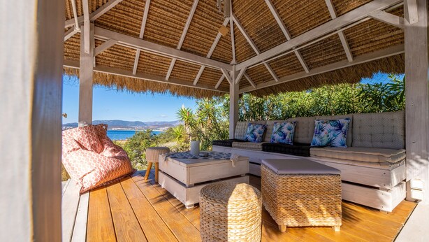 Un espacio de estar al aire libre techado con vistas al mar, terraza de madera y techo de paja.