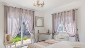 Un dormitorio con cama, una silla, tocador y ventana con cortinas.