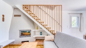 A modern living room with a wooden staircase, a grey sofa, a wooden coffee table, and a white bench.