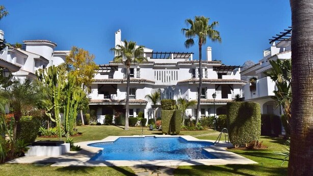 A large, white building with multiple balconies, a swimming pool, and palm trees. - Studio 1 bed 1 bath for 3  *No Terrace* F-3 (Marbella)