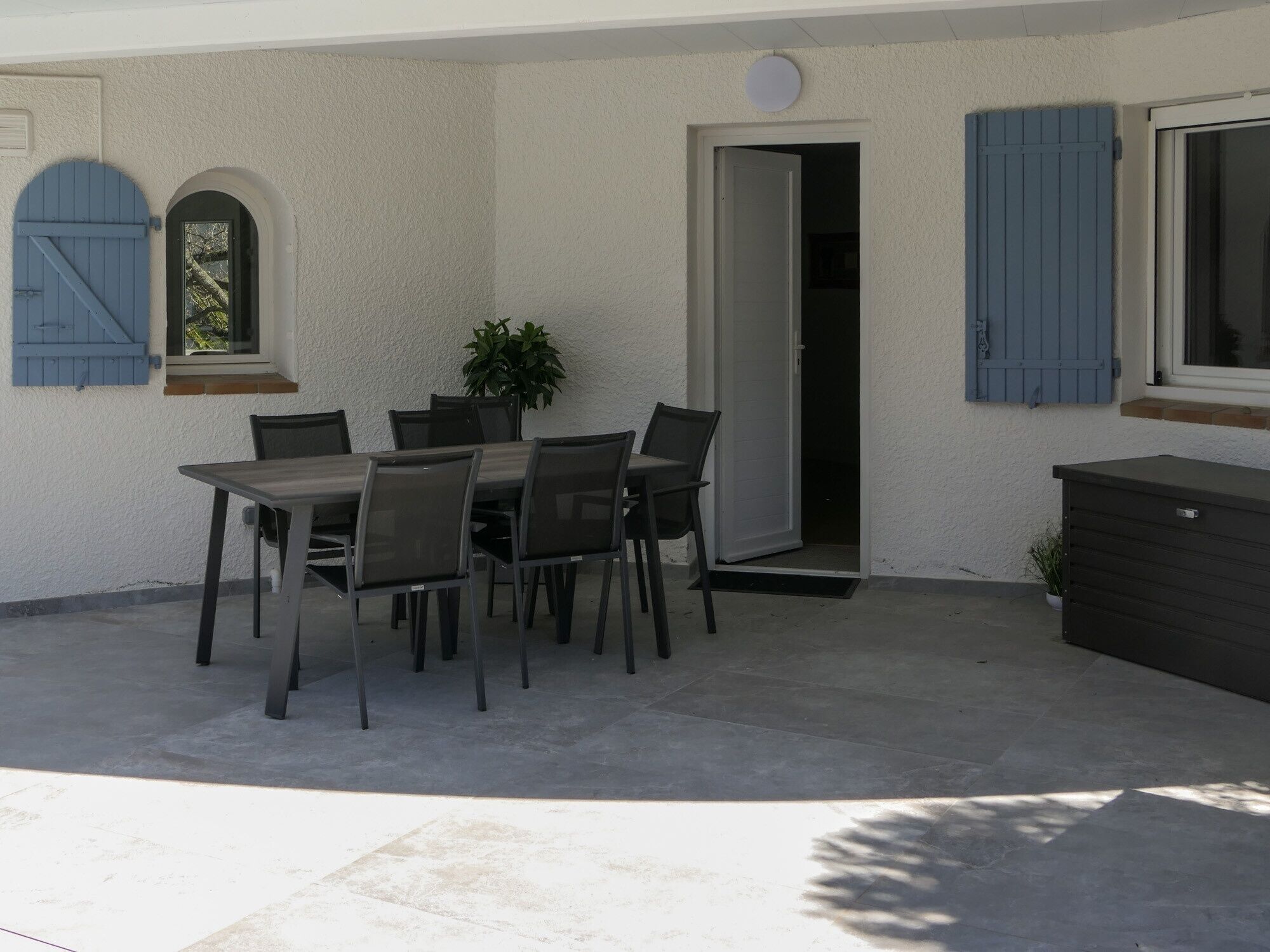 An outdoor patio with a table and chairs, a potted plant, and a sliding door.