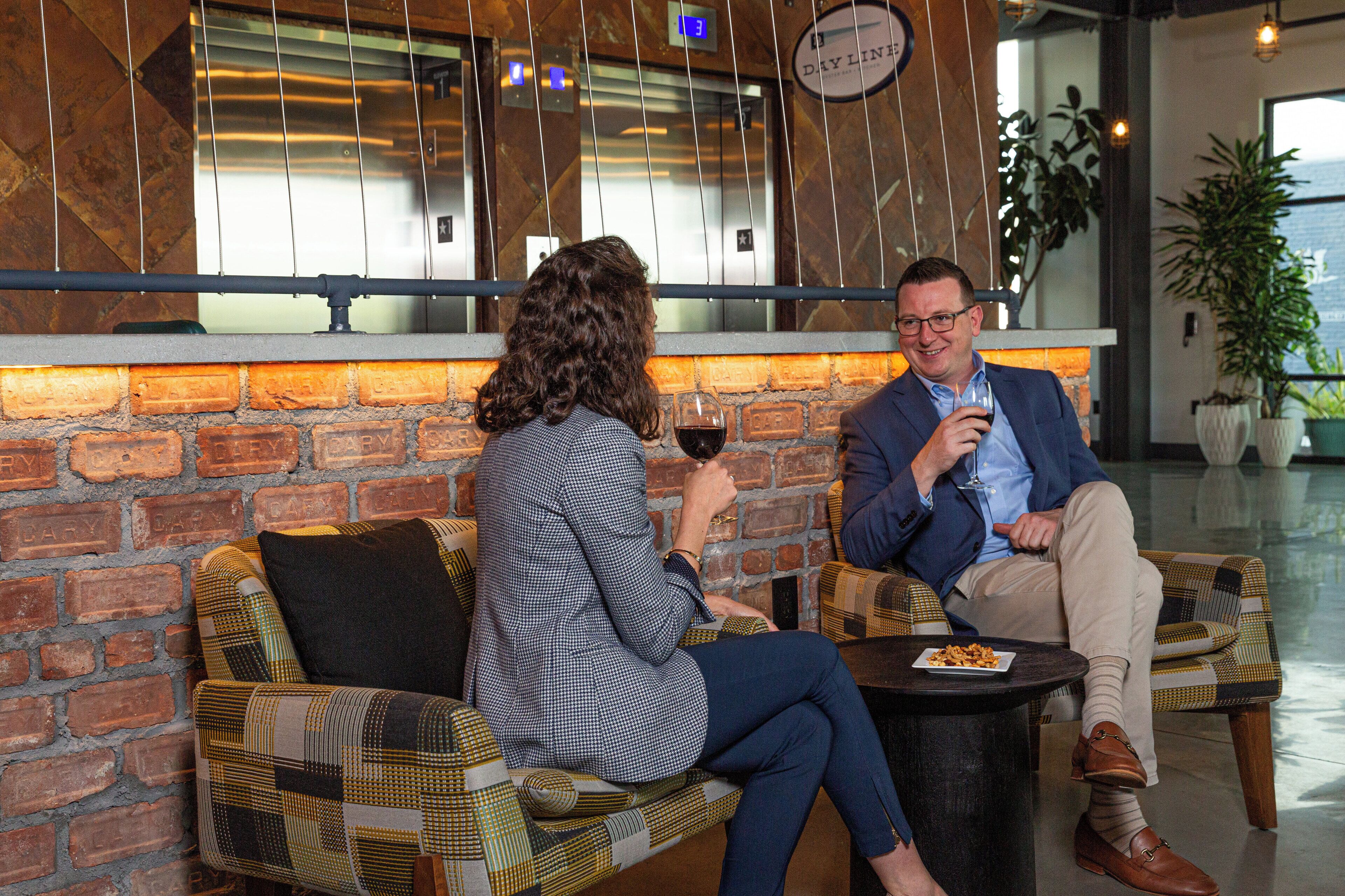 Two people seated on a checkered sofa in a modern interior with a brick wall and a window.