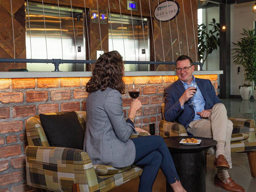 Two people seated on a checkered sofa in a modern interior with a brick wall and a window.
