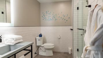 A modern bathroom with a white toilet, a glass shower enclosure, and a sink with stacked towels.