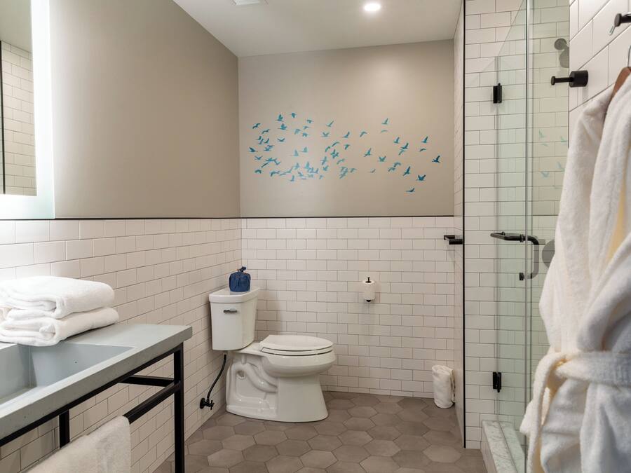 A modern bathroom with a white toilet, a glass shower enclosure, and a sink with stacked towels.