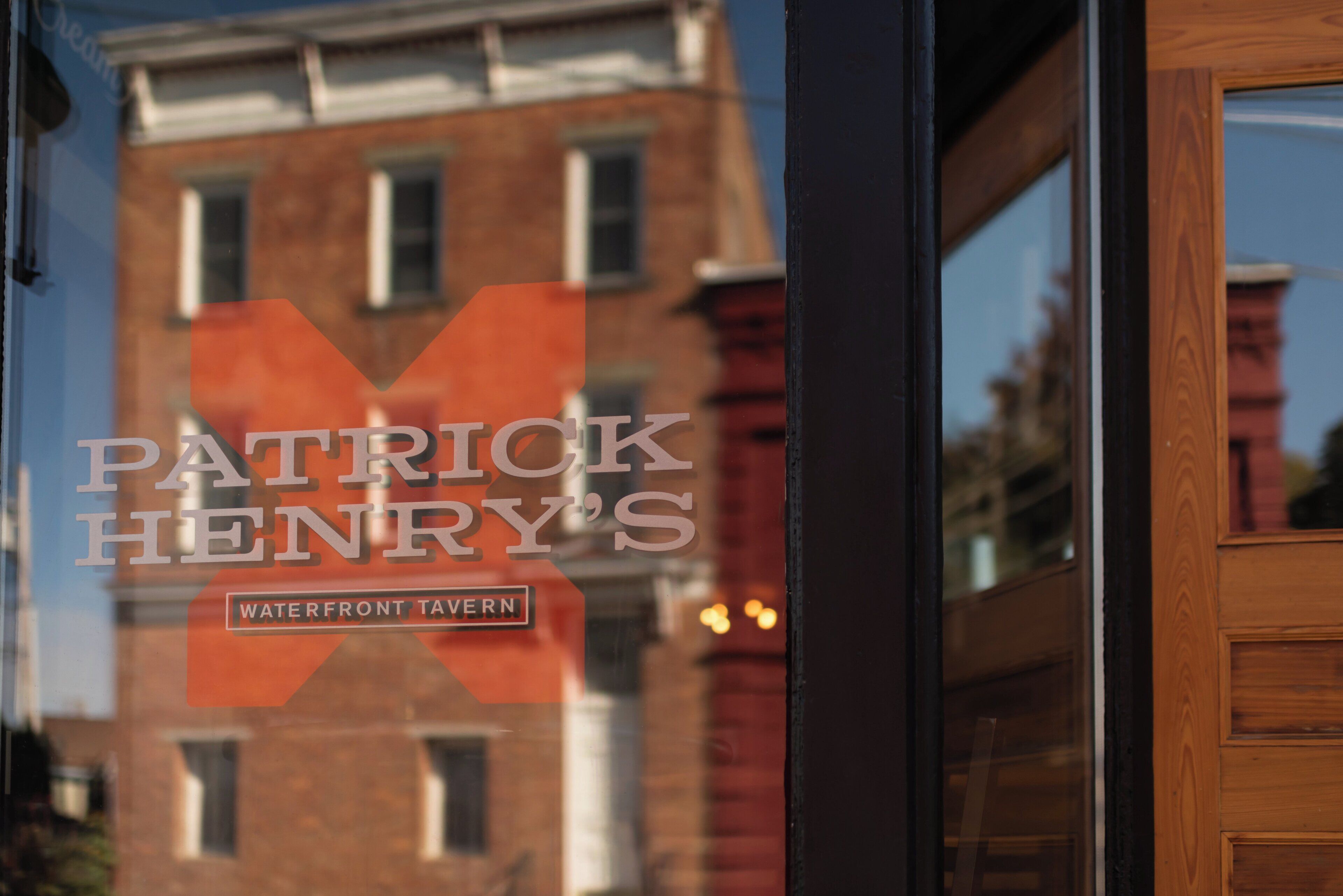 A sign for "Patrick Henry's Waterfront Tavern" with a view of a brick building in the background.