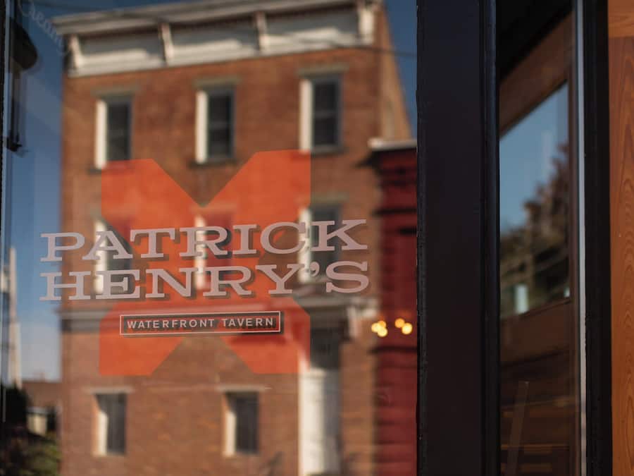 A sign for "Patrick Henry's Waterfront Tavern" with a view of a brick building in the background.