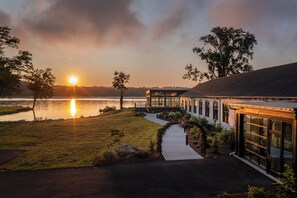 A lakeside property with a glass conservatory, a pathway leading to a building, and a sunset view. - voco James Newbury Hudson Valley by IHG (Coxsackie)