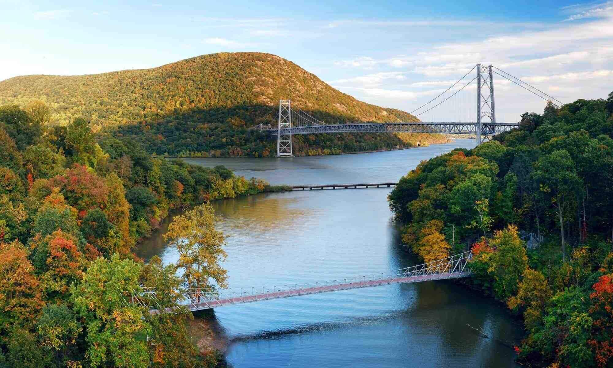 A suspension bridge over a river surrounded by autumn foliage.