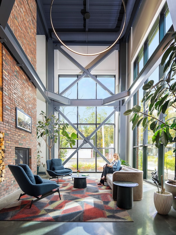 A spacious interior with a high ceiling, exposed brick walls, large windows, and modern furniture.