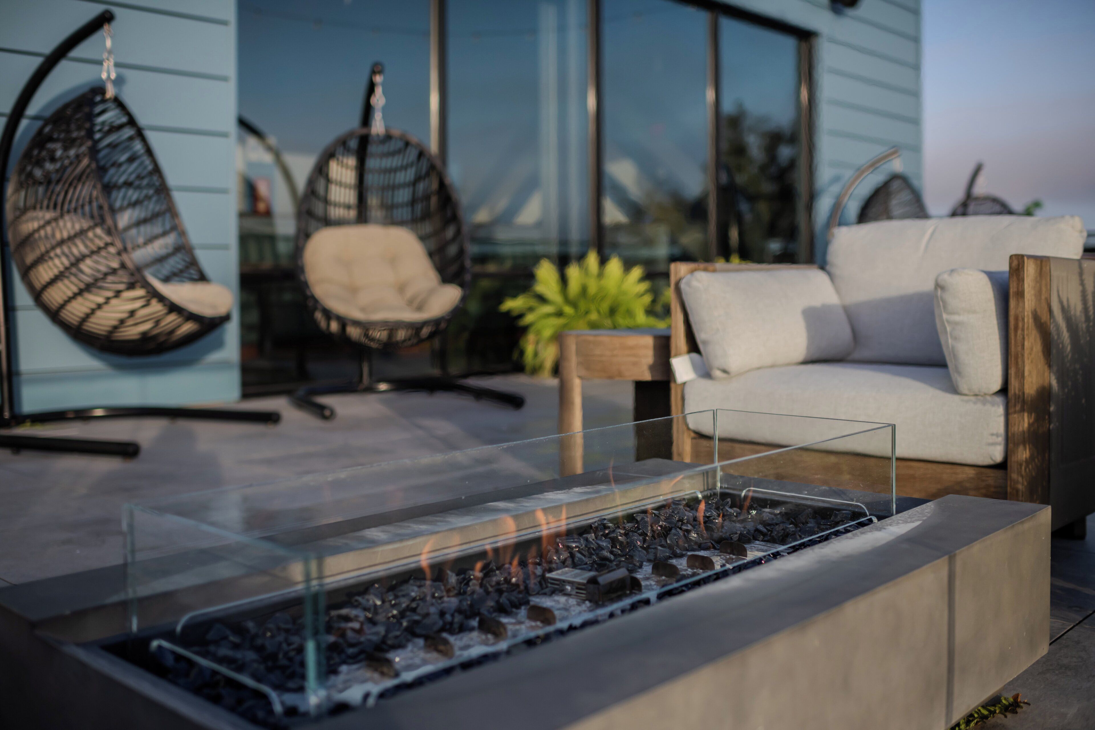 Een modern terras met een vuurkorf met glazen blad, zachte stoelen en een bank.