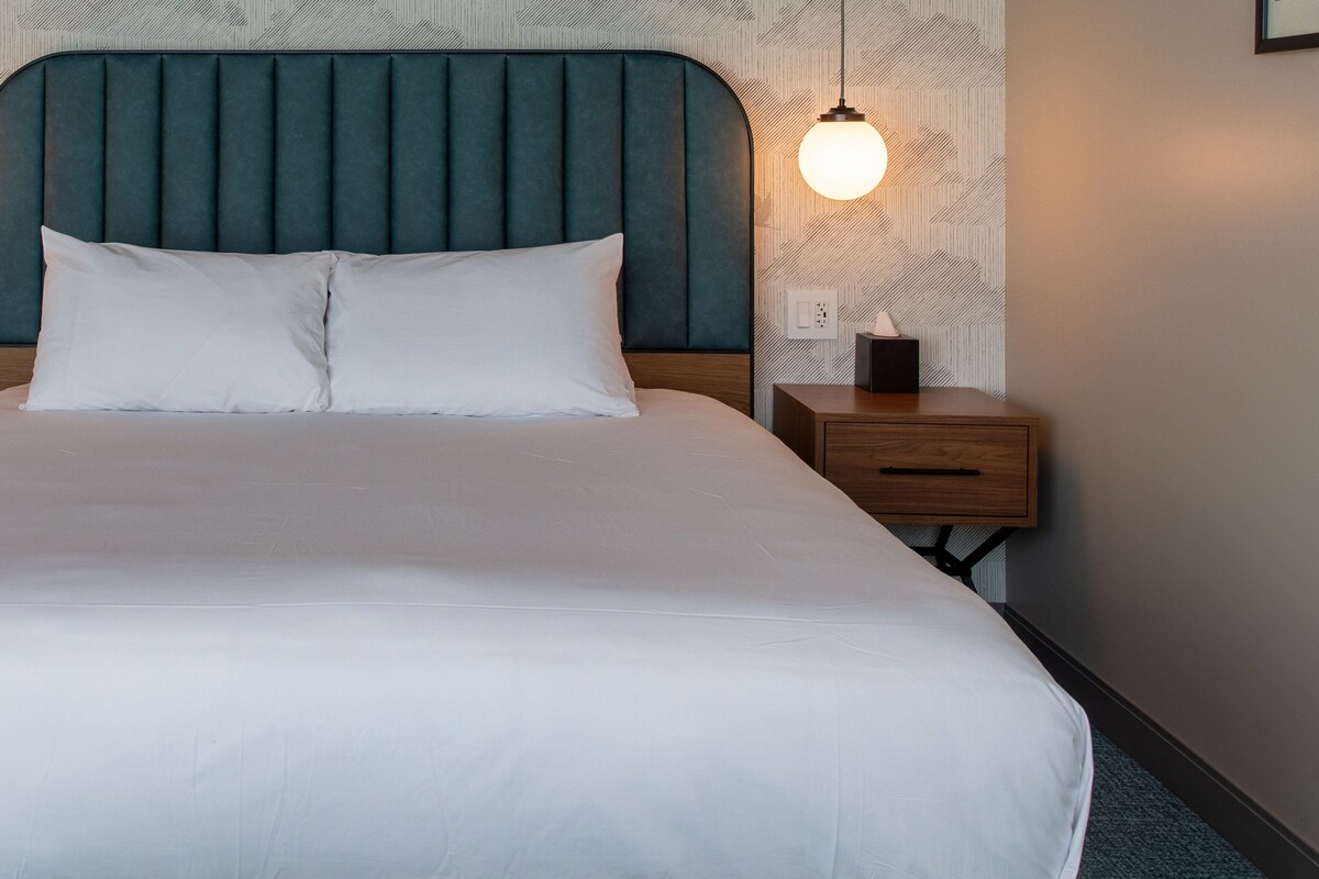 Un lit bien fait, avec une tête de lit, une table de chevet avec une lampe et un mur décoré d’un motif.