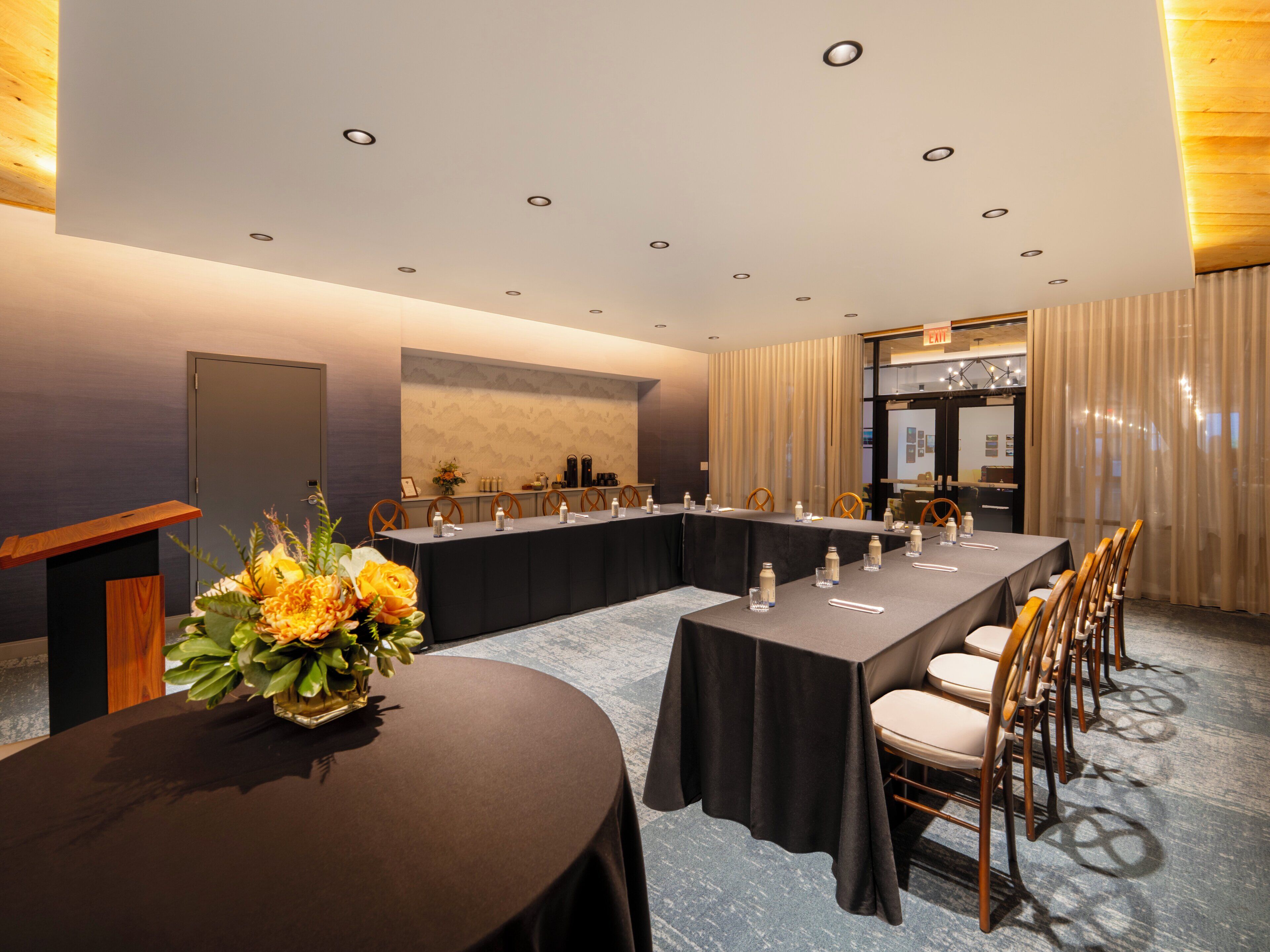Ein Konferenzraum mit langem Tisch, Stühlen, einem Rednerpult und einer Blumenkomposition.