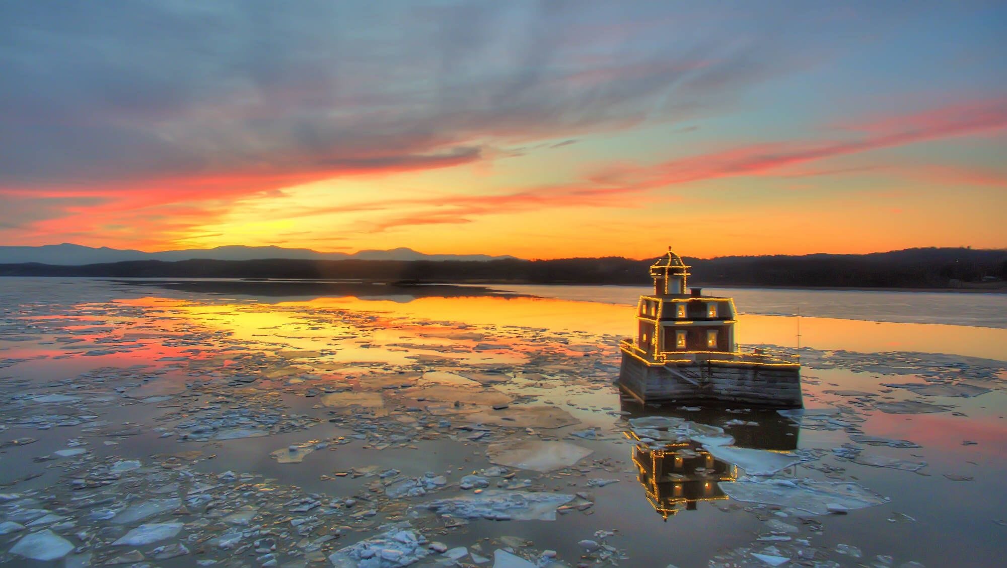 A lighthouse on a frozen body of water with a sunset in the background.