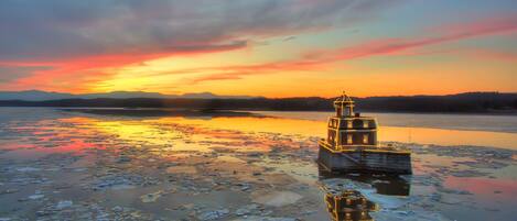 A lighthouse on a frozen body of water with a sunset in the background.