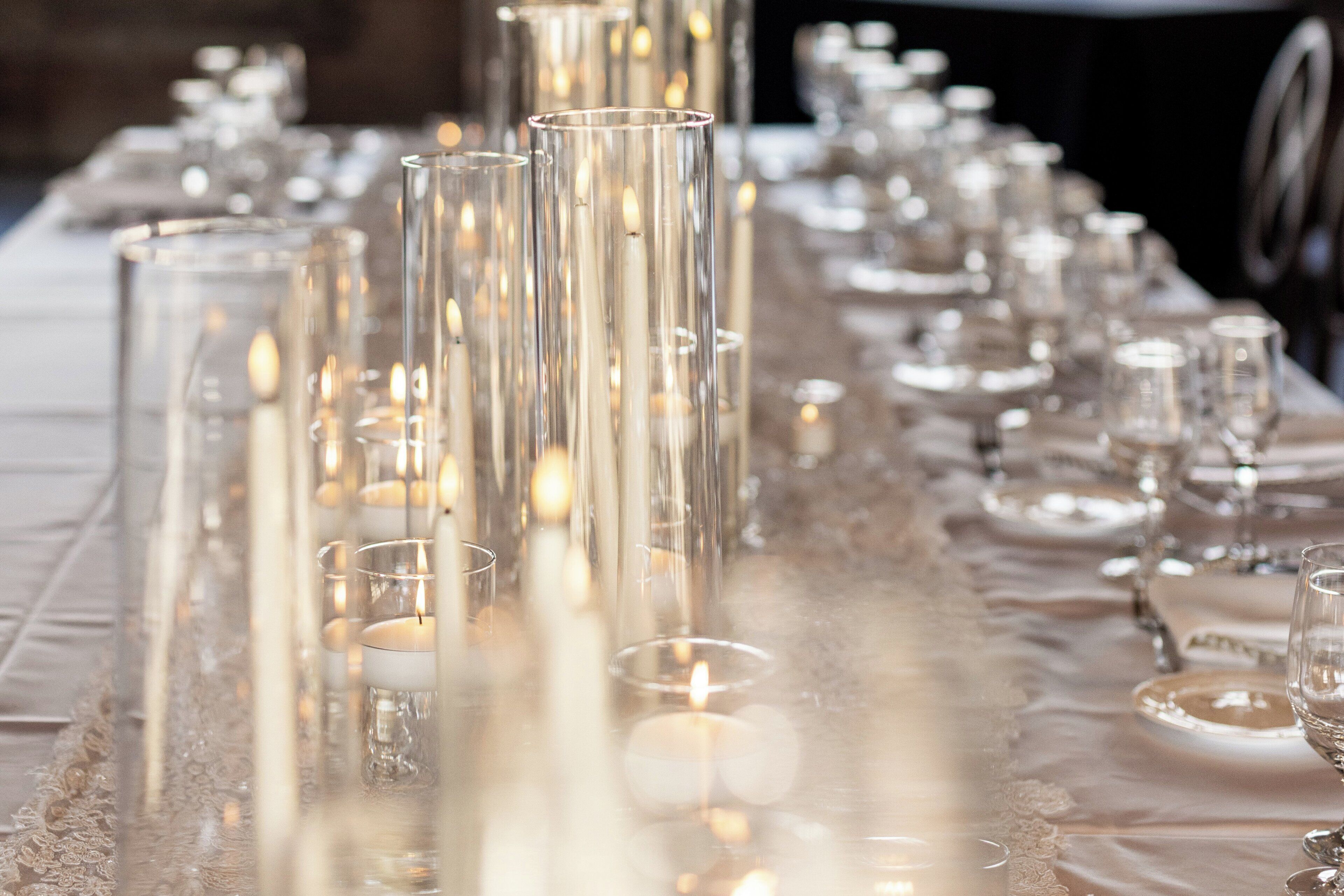 Una larga mesa dispuesta con velas y copas de cristal, evocando un ambiente de cena formal.