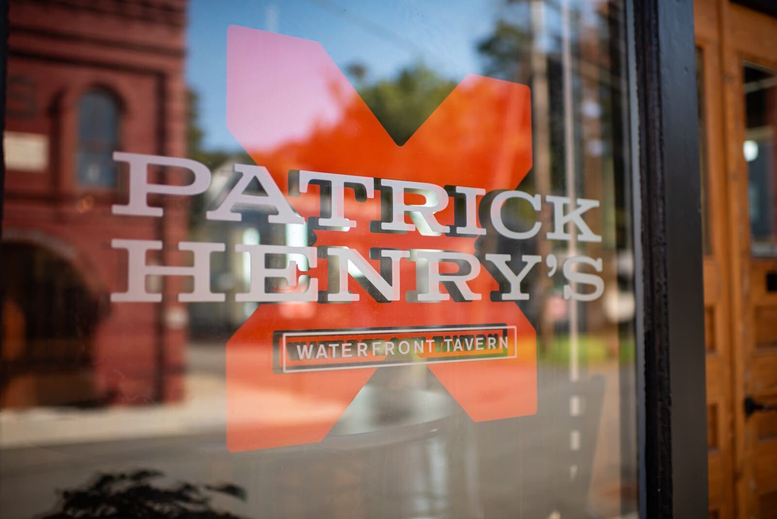 Ein Fenster mit dem Schriftzug "PATRICK HENRY'S WATERFRONT TAVERN" und einem Blick auf ein rotes Gebäude im Hintergrund.