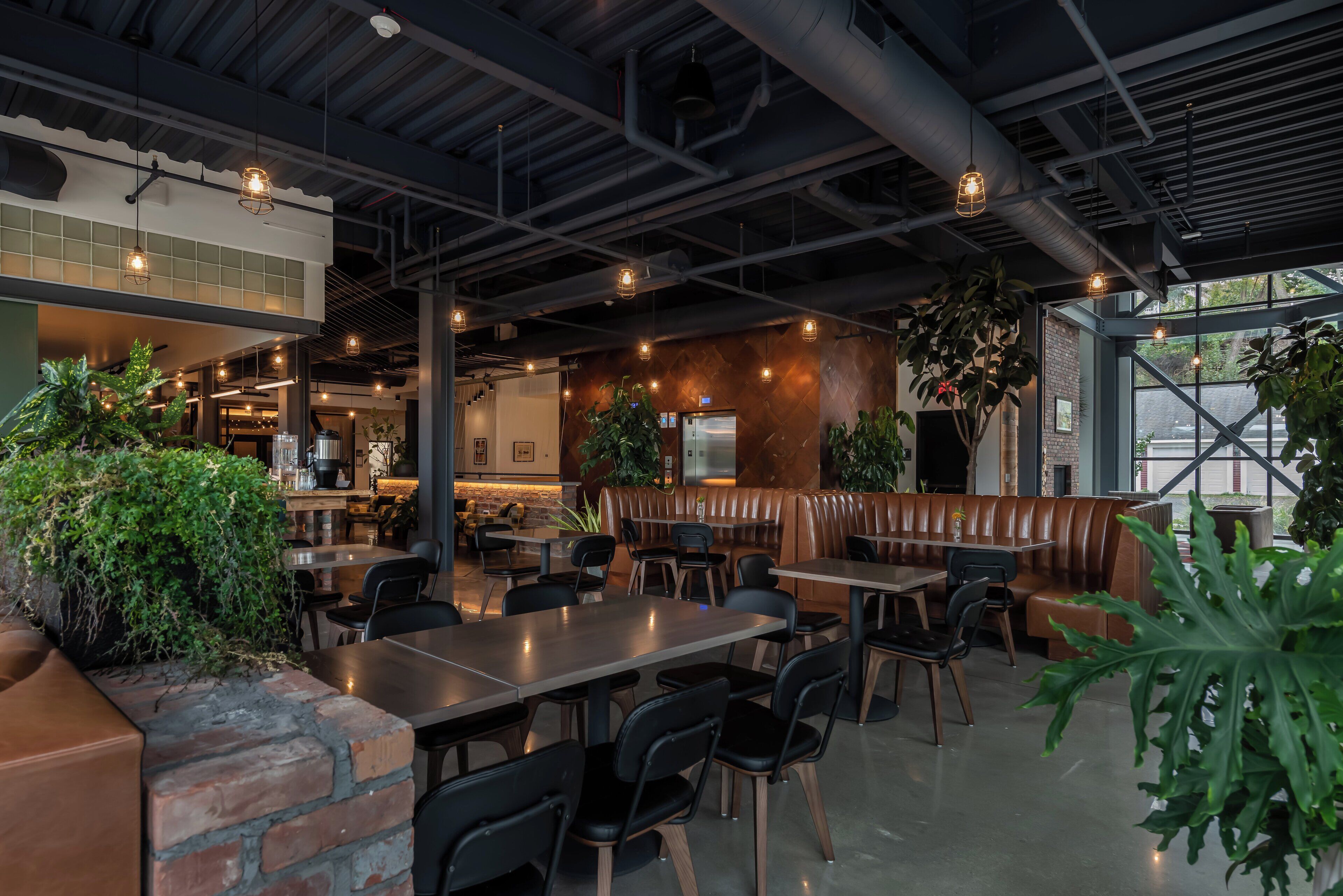 Un restaurante moderno con techos a la vista, iluminación industrial y una variedad de arreglos de asientos, incluyendo cabinas y mesas.