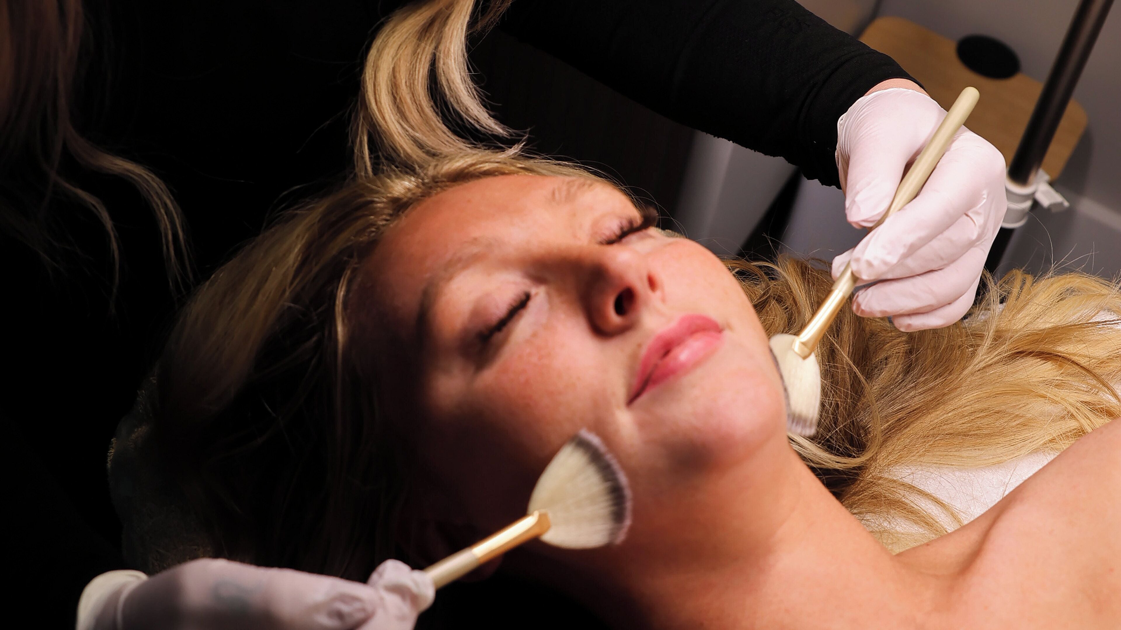Una persona acostada mientras un profesional le aplica un tratamiento facial.