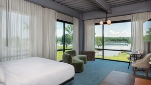 Et moderne hotelværelse med en stor seng, grønne lænestole, et lille bord og udsigt til en sø.